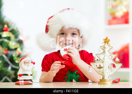 Kleine Mädchen tragen eine festliche rote Weihnachtsmütze mit Weihnachtsgebäck Stockfoto