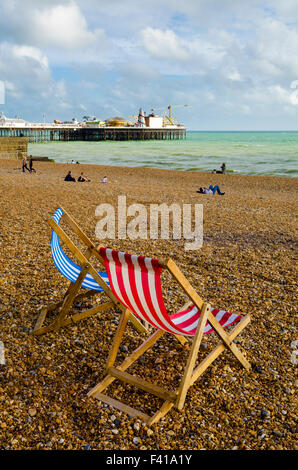 Zwei Liegestühle auf dem einzigen Strand in Brighton und Hove mit Brighton Pier in der Ferne, East Sussex, England. Stockfoto