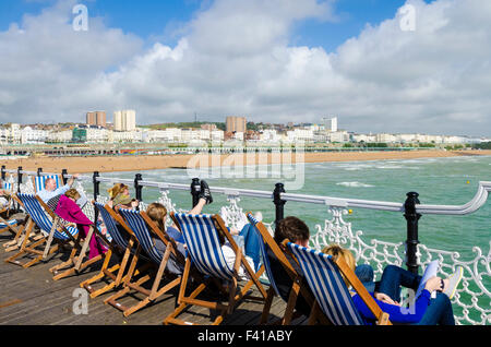 Leute sitzen in Liegestühlen auf Brighton Pier mit Blick auf das Meer und den Strand von Brighton. East Sussex, England. Stockfoto