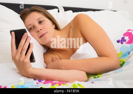 junge Frau überprüft ihr Telefon im Bett Stockfoto