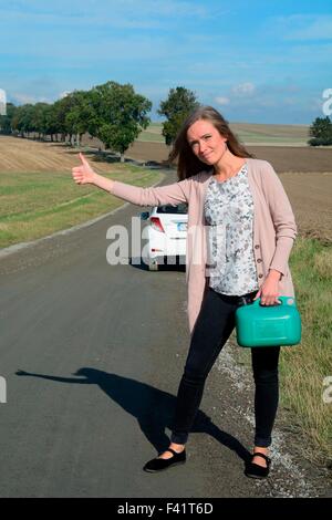 Junge Brünette Frau mit einem Benzin kann per Anhalter auf einer leeren Landstraße, Krageholm, Skåne, Südschweden, Schweden Stockfoto