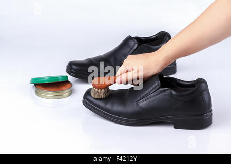 zarte Frauenhand Polieren Schwarze Lederschuhe mit Schuhbürste auf weißem Hintergrund Stockfoto