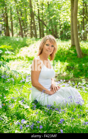 Frau sitzt unter den Glockenblumen im Wald in UK Stockfoto