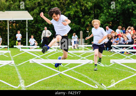 Englisch Schule Sport Tag. Kinder, Jungen, 10-11 Jahre alt, springen über Hürden während des Rennens, auf Sport im freien Feld, racing in Richtung Betrachter. Stockfoto