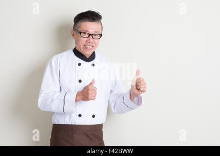 Porträt der 50er Jahre reife asiatische männlichen Chef in Uniform Daumen aufgeben, auf einfarbigen Hintergrund mit Schatten, Textfreiraum stehen. Stockfoto