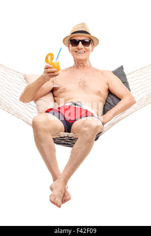 Freudige Senior in roten Badehose liegen in einer Hängematte und trinken einen orangenen cocktail isolierten auf weißen Hintergrund Stockfoto