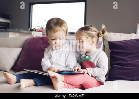 Junge Geschwister betrachten Buch zusammen auf sofa Stockfoto