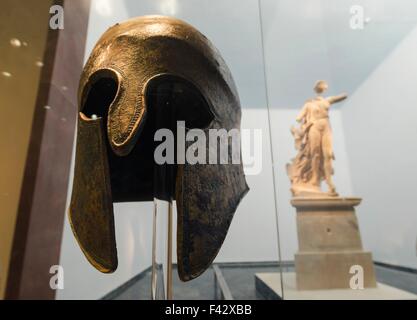 Eine Nahaufnahme von einem original antiken griechischen Helm und die Statue der Göttin Nike, der Göttin des Sieges, im Hintergrund. Ein Gedanke Stockfoto