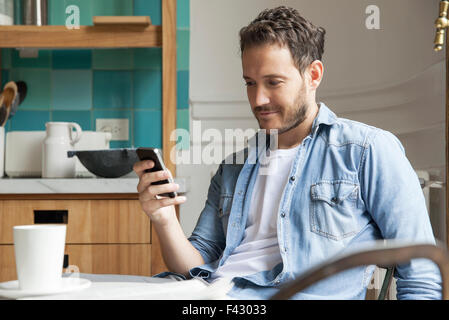 Mann liest Nachrichten auf Smartphone beim Frühstück Stockfoto