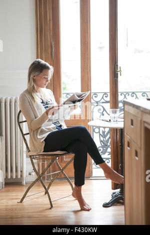 Junge Frau, die Zeitung zu Hause lesen Stockfoto