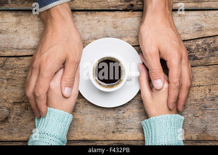 Mann hält in der Nähe von einer Tasse Kaffee Draufsicht Bild auf hölzernen Hintergrund Frauenhand. Freundschaft Kaffee Hintergrund Stockfoto