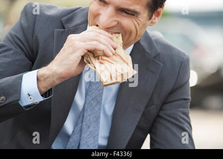 Geschäftsmann unterwegs Sandwich zu essen Stockfoto