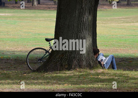 Mann mit Fahrrad sitzt Lesung gegen einen Baum im Prospect Park in Brooklyn Stockfoto