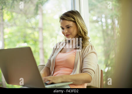 Eine Frau sitzt mit einem Laptop auf einer Veranda sitzen. Stockfoto