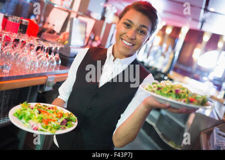 Hübsche Kellnerin hält Teller mit Salaten Stockfoto