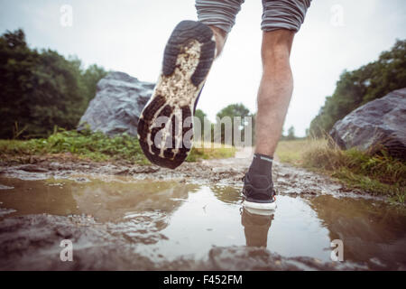 Mann durch Schlammpfützen Joggen Stockfoto