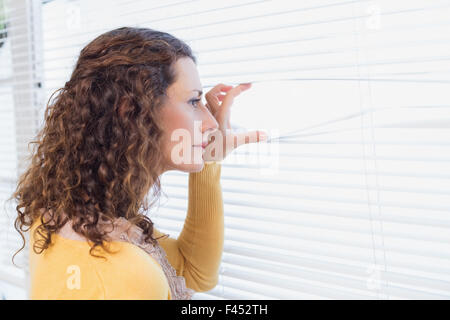 Neugierige Frau, die durch Jalousien Stockfoto