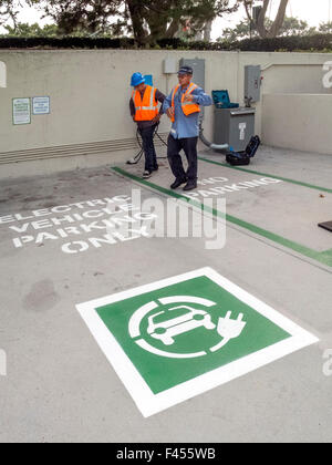 -Reparatur-Techniker pflegen ein Elektroauto Ladestation an einem Irvine, CA, Krankenhaus-Parkplatz. Symbolische Notizsymbol im Vordergrund. Stockfoto