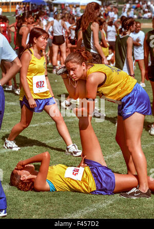 Eine Teen High School Mädchen hilft einen Freund ihre Beine, nach einem wettbewerbsfähigen Wettlauf in Irvine, CA. Hinweis andere Läufer im Hintergrund dehnen dehnen. Stockfoto