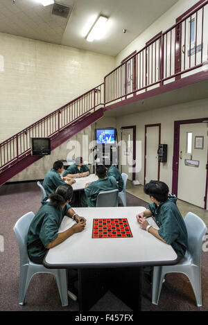 Uniformierte Hispanic teenage Insassen einer Justizanstalt für Orange, CA, spielen Dame in den Aufenthaltsraum. Beachten Sie Fernsehen. Stockfoto