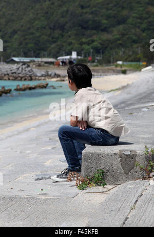 Es ist ein Foto eines kleinen Jungen, der auf die Skyline, Landschaft oder das Meer sucht. Er sitzt auf einem Betonklotz am Strand Stockfoto