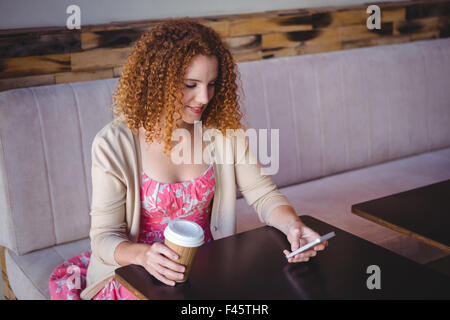 Glücklich lächelnde Frau mit ihrem Smartphone und Kaffee trinken Stockfoto