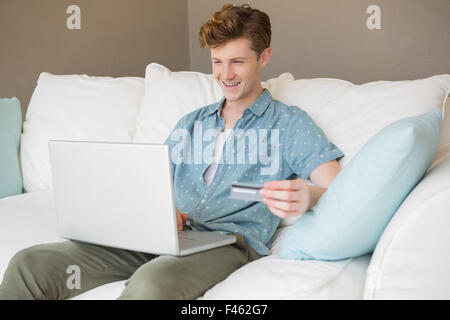 Glücklich Jüngling sitzt auf dem Sofa Online-shopping mit laptop Stockfoto