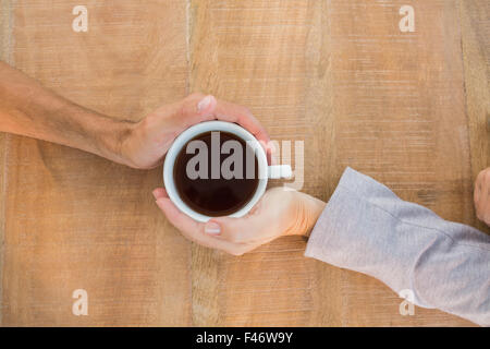 Zwei Hände halten eine Tasse Kaffee auf Holztisch Stockfoto
