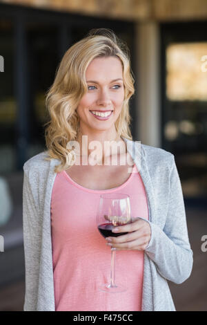 Lächelnde blonde Frau stehen und halten Weinglas Stockfoto