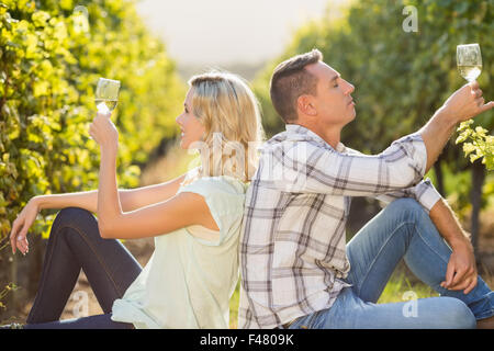 Lächelnde paar sitzen Rücken an Rücken mit Weinglas neben Weinrebe Stockfoto