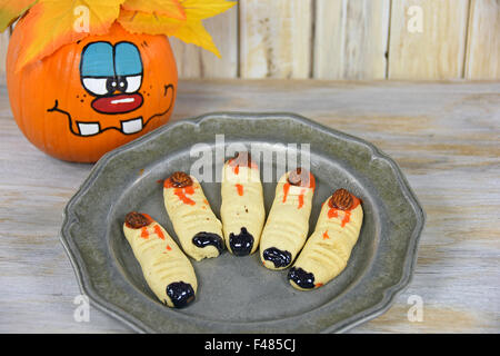 Halloween-Finger-Plätzchen mit lustigen Gesicht gemalt auf Herbst Kürbis. Stockfoto