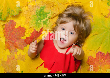 Kind im roten Kleid in gelbe Blätter. Stockfoto