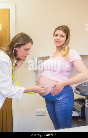 Junger Arzt überprüft ihre lächelnden schwangeren Patientin Stockfoto