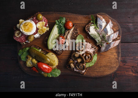 Verschiedene belegte Brötchen dichten, dunklen Roggen Butterbrot mit verschiedenen Belägen. Dänische Smorrebrods auf hölzernen Hintergrund. Noch Stockfoto