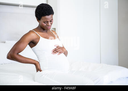 Lächelnde schwangere Frau sitzt auf ihrem Bett Stockfoto