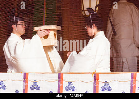 Nishinomiya Schrein, Japan, Priester Zeremonie in Honden, ein Priester, kannushi, vorbei an Heiligen, zum Anderen. Beide tragen Kammuri. Durch Bildschirm gesehen. Stockfoto