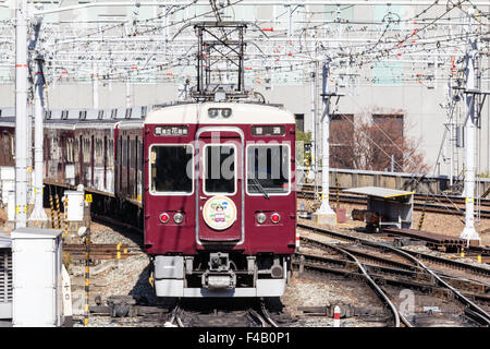 Japan, Osaka Umeda. Private Hankyu Eisenbahn, kastanienbraun gefärbt Zug mit Emblem Abzeichen, kommend in Richtung Betrachter auf Titel mit obenliegenden elektrischen Drähten. Stockfoto