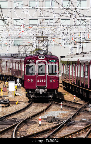 Japan, Osaka Umeda. Private Hankyu Eisenbahn, kastanienbraun gefärbt semi Express Zug in Richtung Betrachter auf Titel mit obenliegenden elektrischen Drähten. Stockfoto