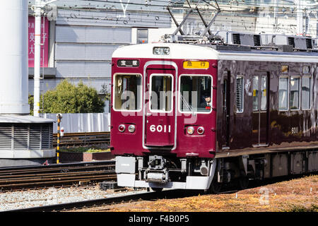 Japan, Osaka Umeda. Private Hankyu Eisenbahn, kastanienbraun gefärbt Express Zug in Richtung Betrachter auf Titel mit obenliegenden elektrischen Drähten. Stockfoto