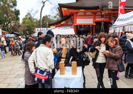 Kyoto, Yasaka Schrein, an Neujahr, am Shogatsu. Die Leute schütteln Holzkisten ihre Omikuji, fortune Papier zu bekommen. Belebte Szene, überfüllt. Stockfoto