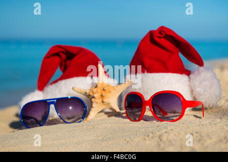 Weihnachtsferien und romantische Silvester am Meer. Santa Hüte und Sonnenbrillen am Sandstrand Stockfoto