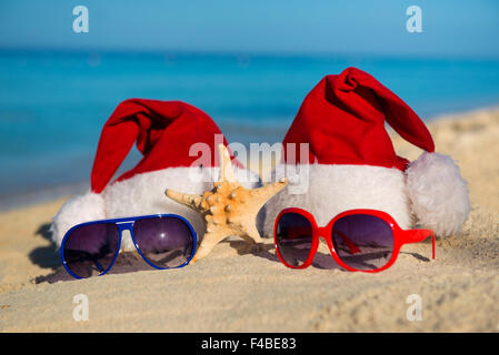 Weihnachtsferien und romantische Silvester am Meer. Santa Hüte und Sonnenbrillen am Sandstrand Stockfoto