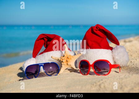 Weihnachtsferien und romantische Silvester am Meer. Santa Hüte und Sonnenbrillen am Sandstrand Stockfoto