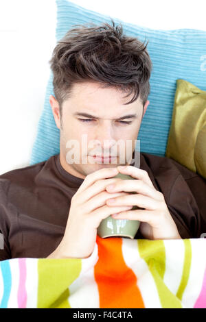 Ill deprimiert Mann hält eine Tasse Kaffee auf dem sofa Stockfoto