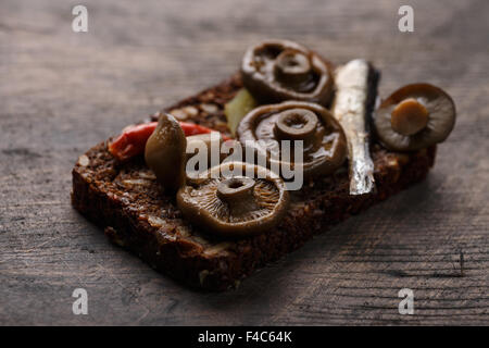 Belegte Brötchen aus dichten Roggen Vollkornbrot (Rugbrod) mit eingelegten Pilzen und Sprotten auf Alter Holzbrett. Selektive Stockfoto