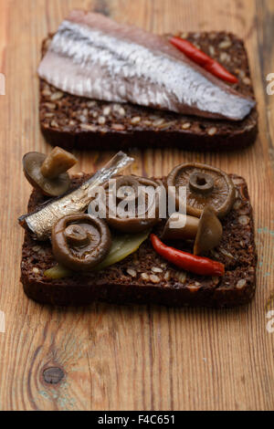Zwei verschiedene öffnen Sandwiches von dichten Roggen Vollkornbrot (Rugbrod) mit eingelegten Pilzen, Sprotten und Herrring auf im Alter Stockfoto