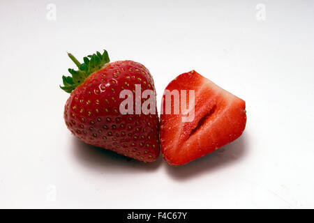 Ein ganzes und eine in Scheiben geschnittene Erdbeeren isoliert auf einem einfachen weißen cyclorama Stockfoto