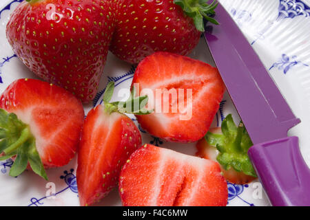 Nahaufnahme der zwei ganze und vier geschnittene Erdbeeren auf einem Teller mit einem Cuttermesser Stockfoto
