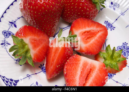 Nahaufnahme der zwei ganze und vier geschnittene Erdbeeren auf einem blau-weißen Teller Stockfoto