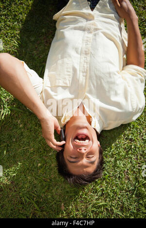 Mann lachen während der Verwendung einer Telefons, wie er im Gras liegt Stockfoto